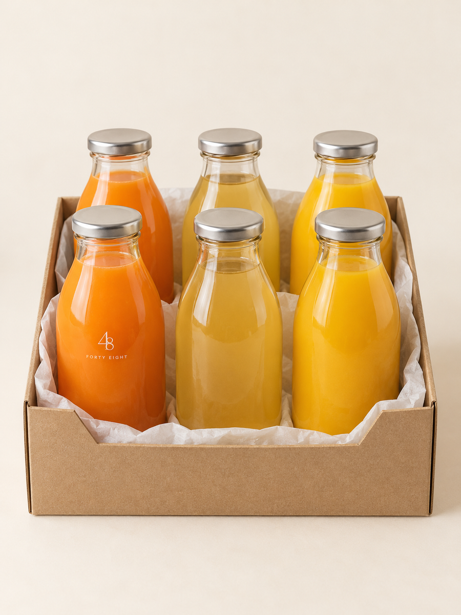 Six clear glass juice bottles in orange, apple and apple-mango tones arranged in a kraft box lined with white baking paper on a cream background, with a small Forty Eight lockup on one bottle.